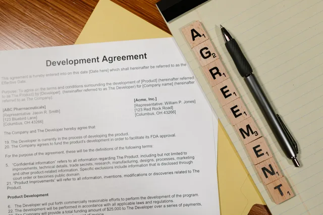 Close-up of a development agreement document with pen and Scrabble tiles spelling 'AGREEMENT.'. Hvordan opsiger man en dansk leverandøraftale korrekt?